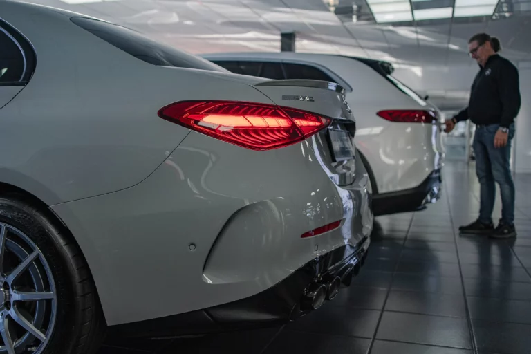 Heck eines weißen Mercedes-Benz im Ausstellungsraum, dahinter ein Mitarbeiter an einem weiteren Fahrzeug
