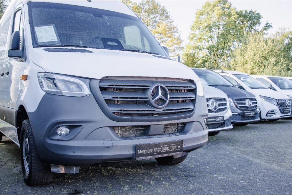 Weißer Mercedes-Benz Sprinter mit Kennzeichenhalter Mercedes-Benz Junge Sterne, dahinter weitere Transporter auf dem Hof