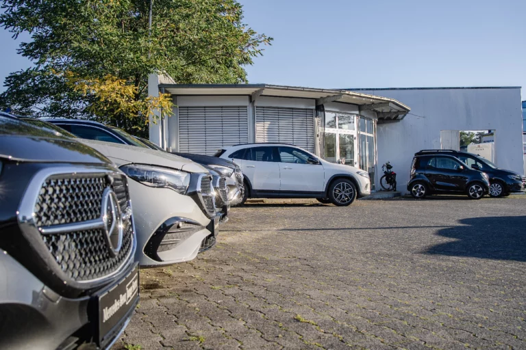 Gebrauchtfahrzeuge auf dem Hof vor dem Autohaus, vorne angeschnitten der Kühlergrill eines Mercedes-Benz