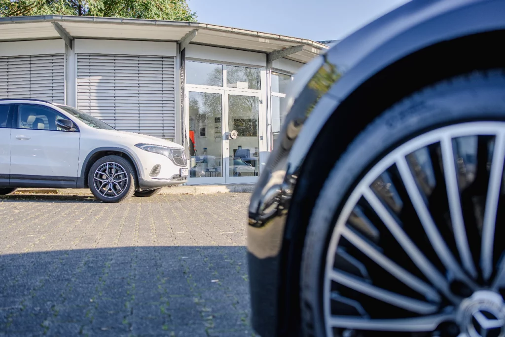 Weißer Mercedes-Benz SUV vor dem Autohaus, im Vordergrund die Felge eines dunklen Mercedes-Benz