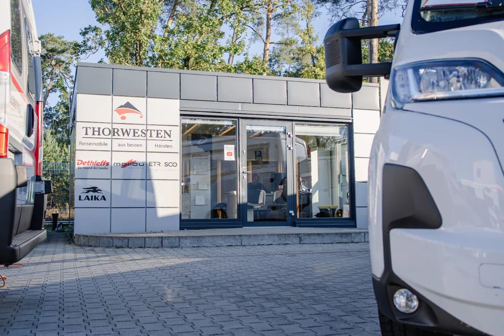 Verkaufsgebäude von Reisemobile Thorwesten mit den Markenschildern Dethleffs, Malibu, Etrusco und Laika, rechts angeschnitten ein weißes Reisemobil
