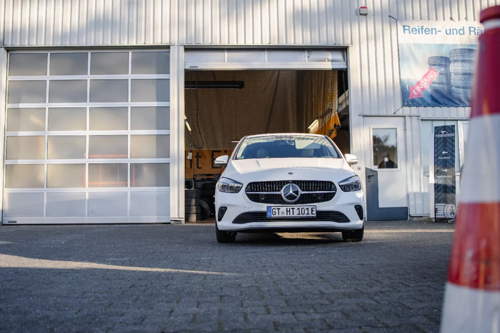 Weißer Mercedes-Benz vor dem geöffneten Tor der Reifen- und Räderwerkstatt