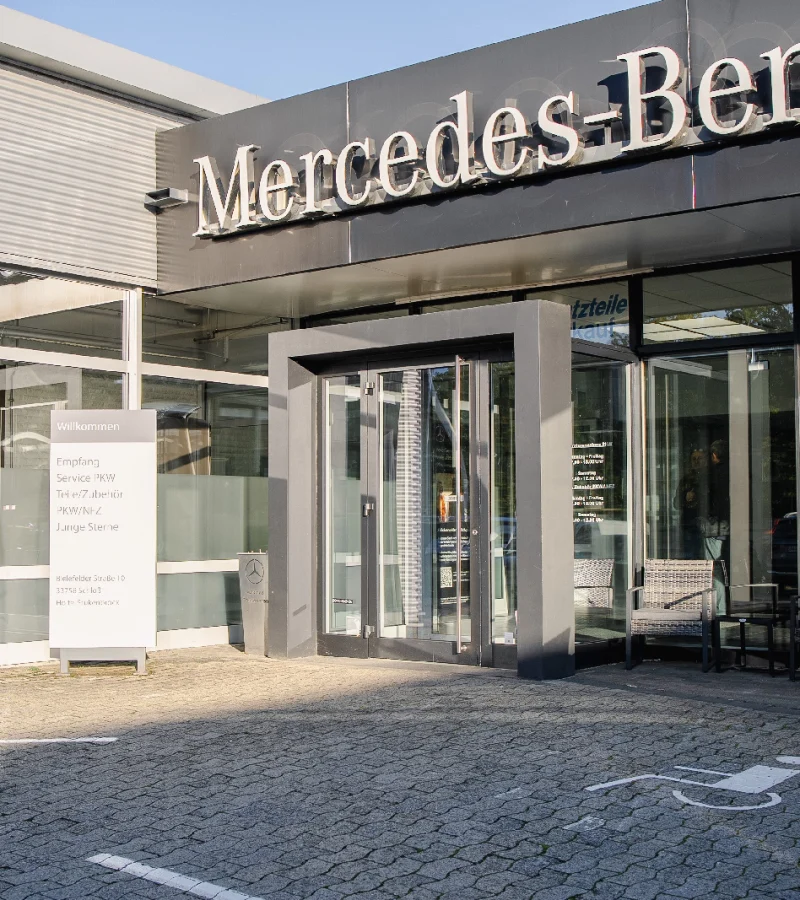 Eingang des Autohauses mit Mercedes-Benz Schriftzug, davor ein Parkplatz mit Rollstuhlsymbol