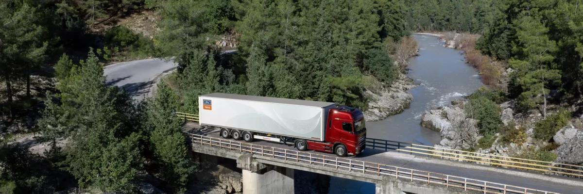 Luftaufnahme: Sattelzug mit rotem Fahrerhaus und weißem Auflieger auf einer Brücke über einen Fluss